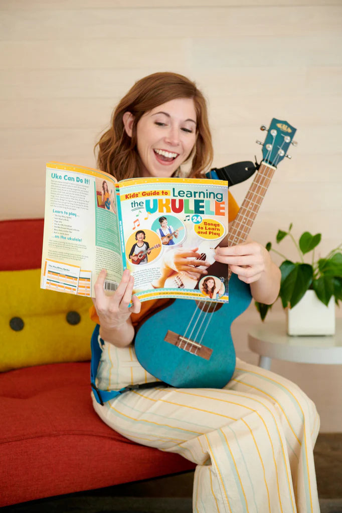 Emily Arrow smiling while holding ukulele and reading Kid's Guide to Learning the Ukulele Book