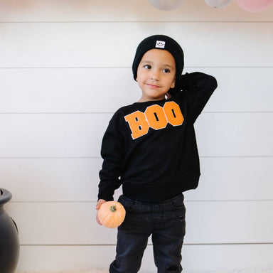 Child wearing black sweatshirt with embroidered orange letters spelling out BOO
