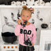 Girl wearing pink sweatshirt with black BOO patch playing with pretend black phone