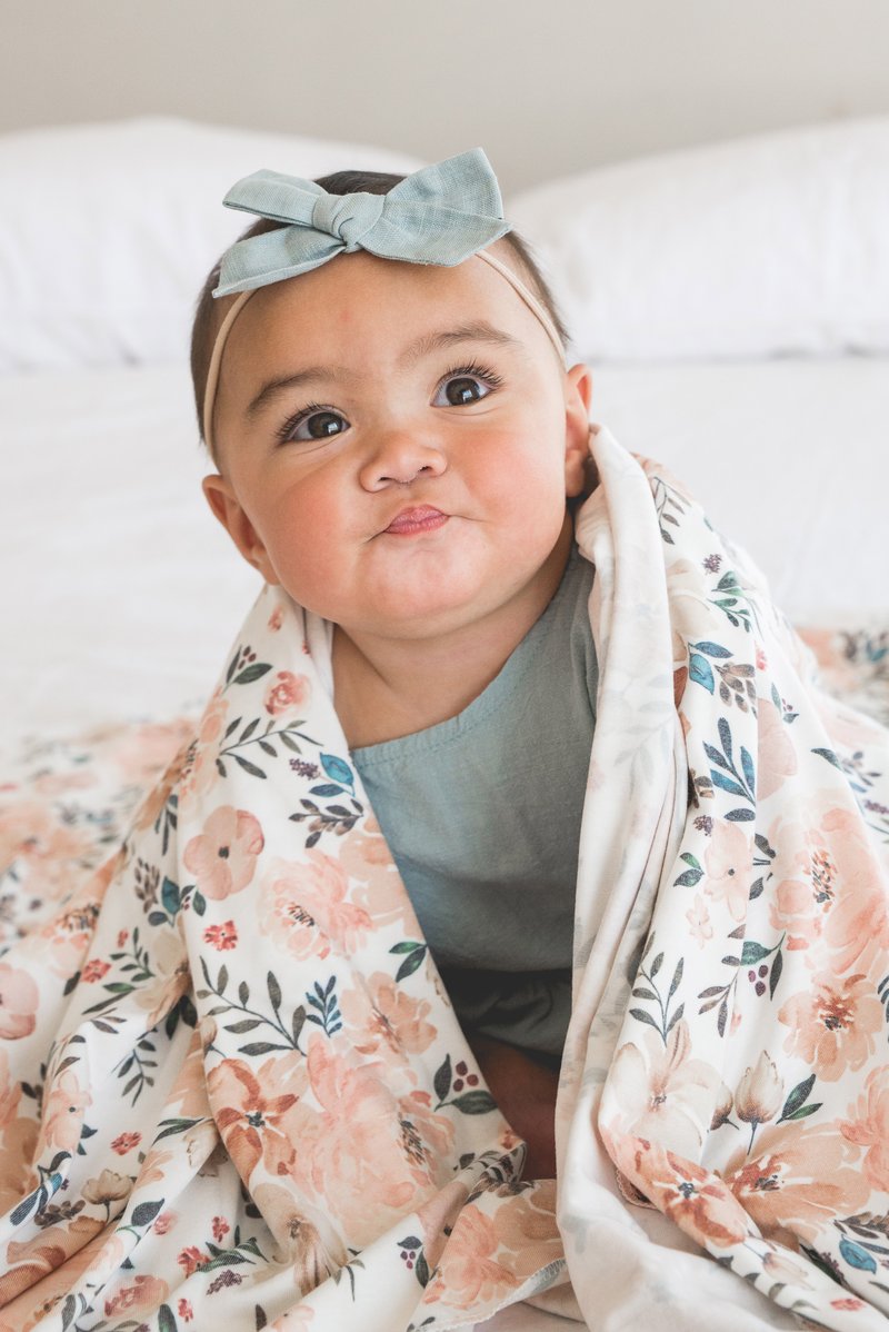 baby with blanket around shoulders wearing matching blue bow