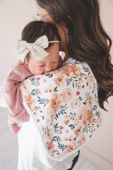 baby resting on womans shoulder laying on floral burp cloth