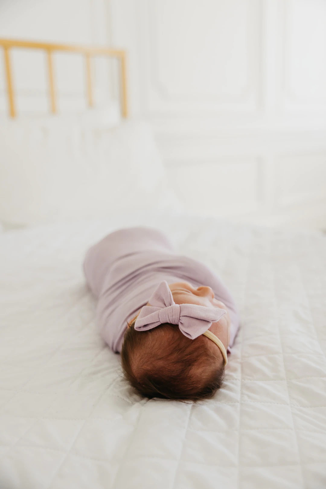 baby wearing purple bow wrapped in matching blanket