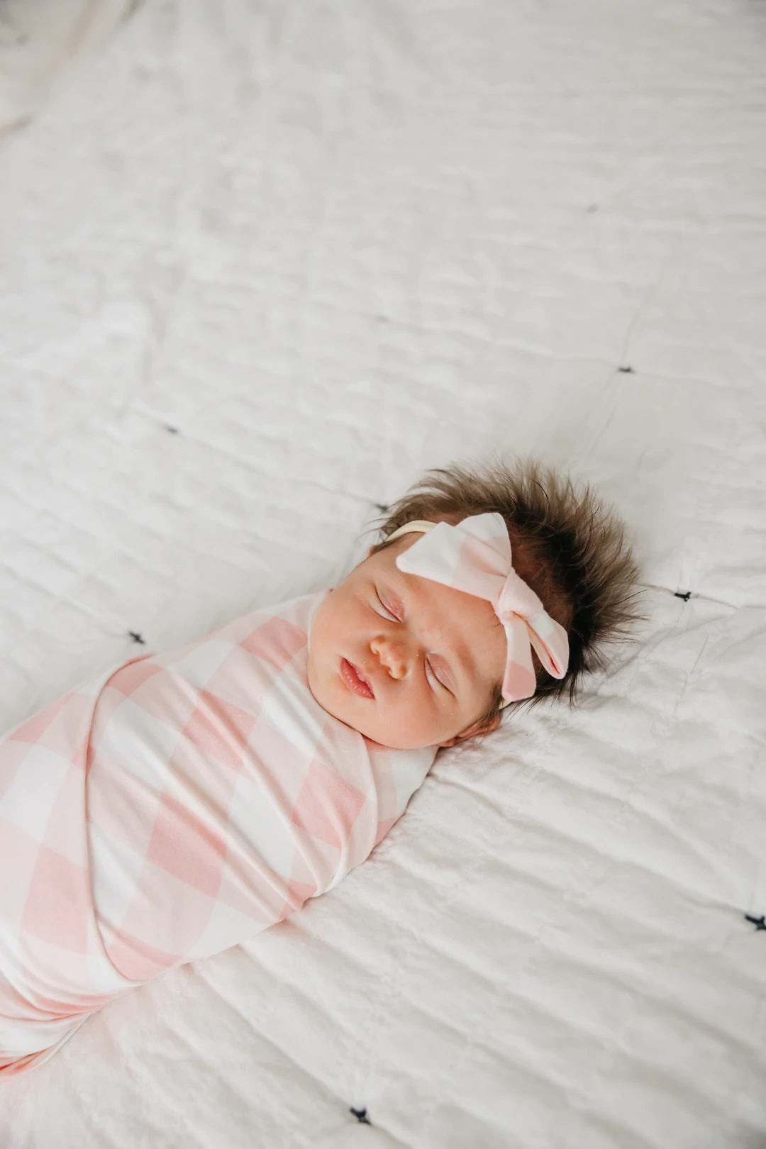 newborn baby wearing bow and wrapped in matching blanket